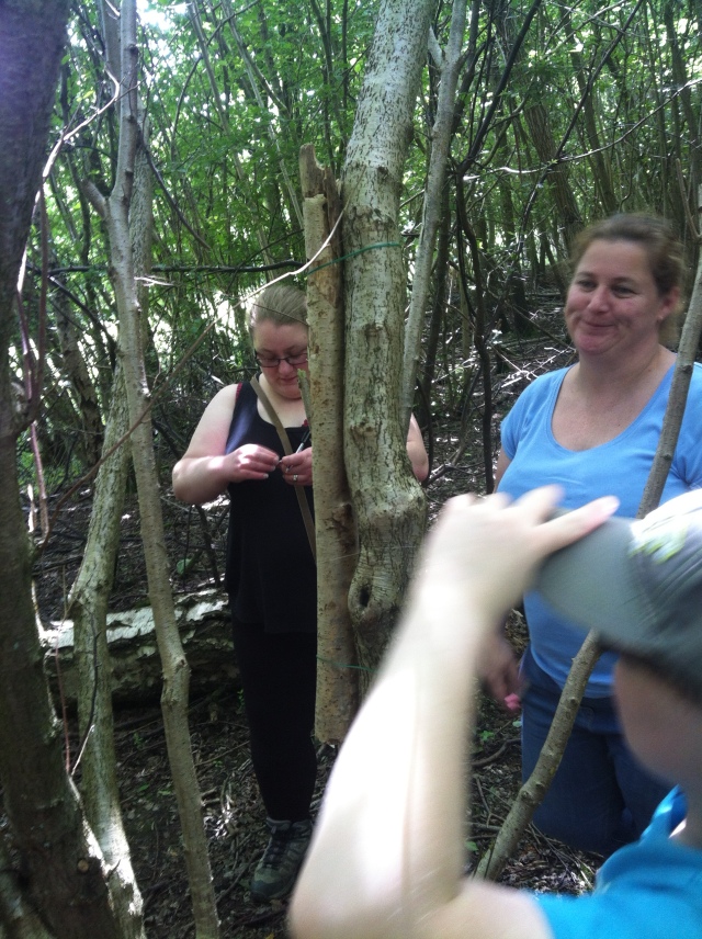 The cache is hidden inside a thin branch that has been attached to another branch using fishing line. Shar inspects the cache as Sam and Melissa look on.