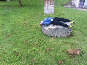 Sam lays on the lump of pudding stone in the Churchyard