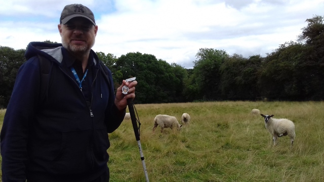 Paul stands in a field holding the Jimmy Talon TB while a sheep looks on.